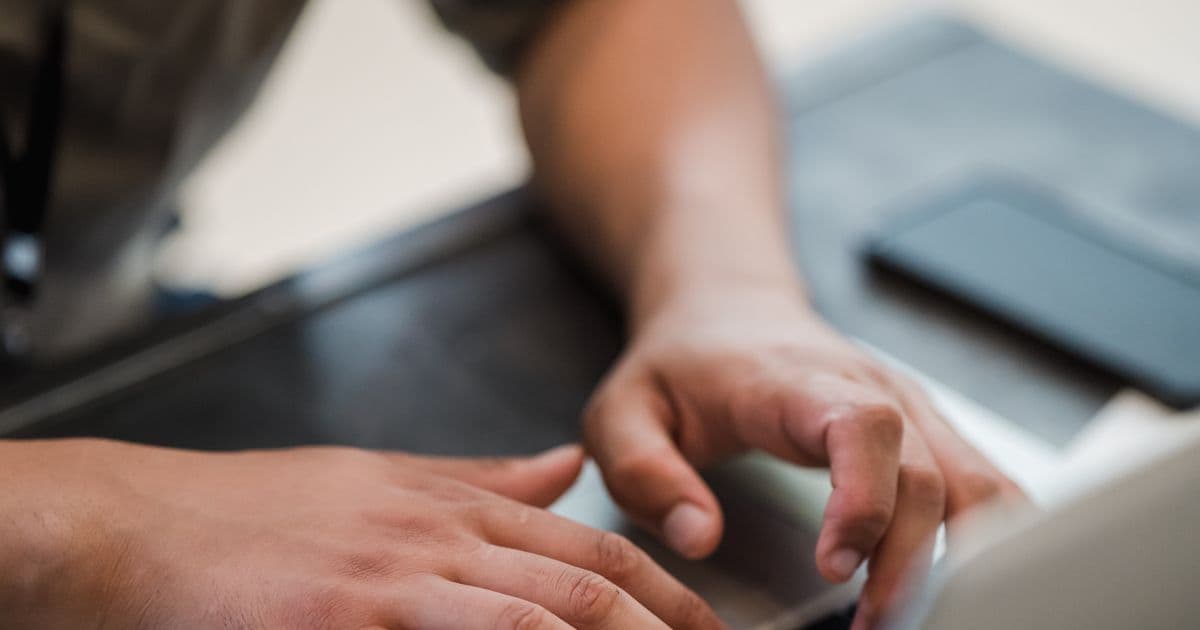 Close-up of two hands typing on a laptop keyboard beside a phone