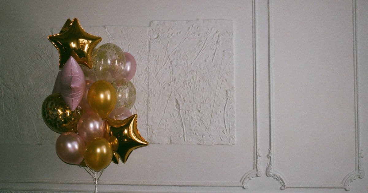 Gold and pink balloon bouquet with star balloons against a plain white wall